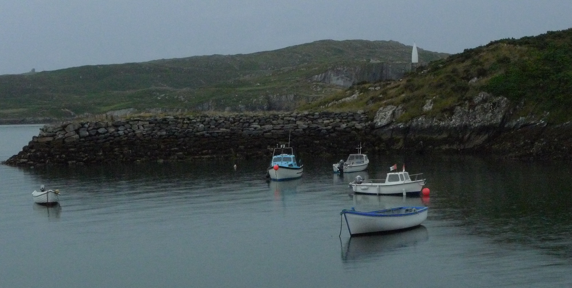Fishing boats moored in Baltimore harbour, West Cork, with the white Baltimore Beacon ('Lot's Wife') on the headland beyond