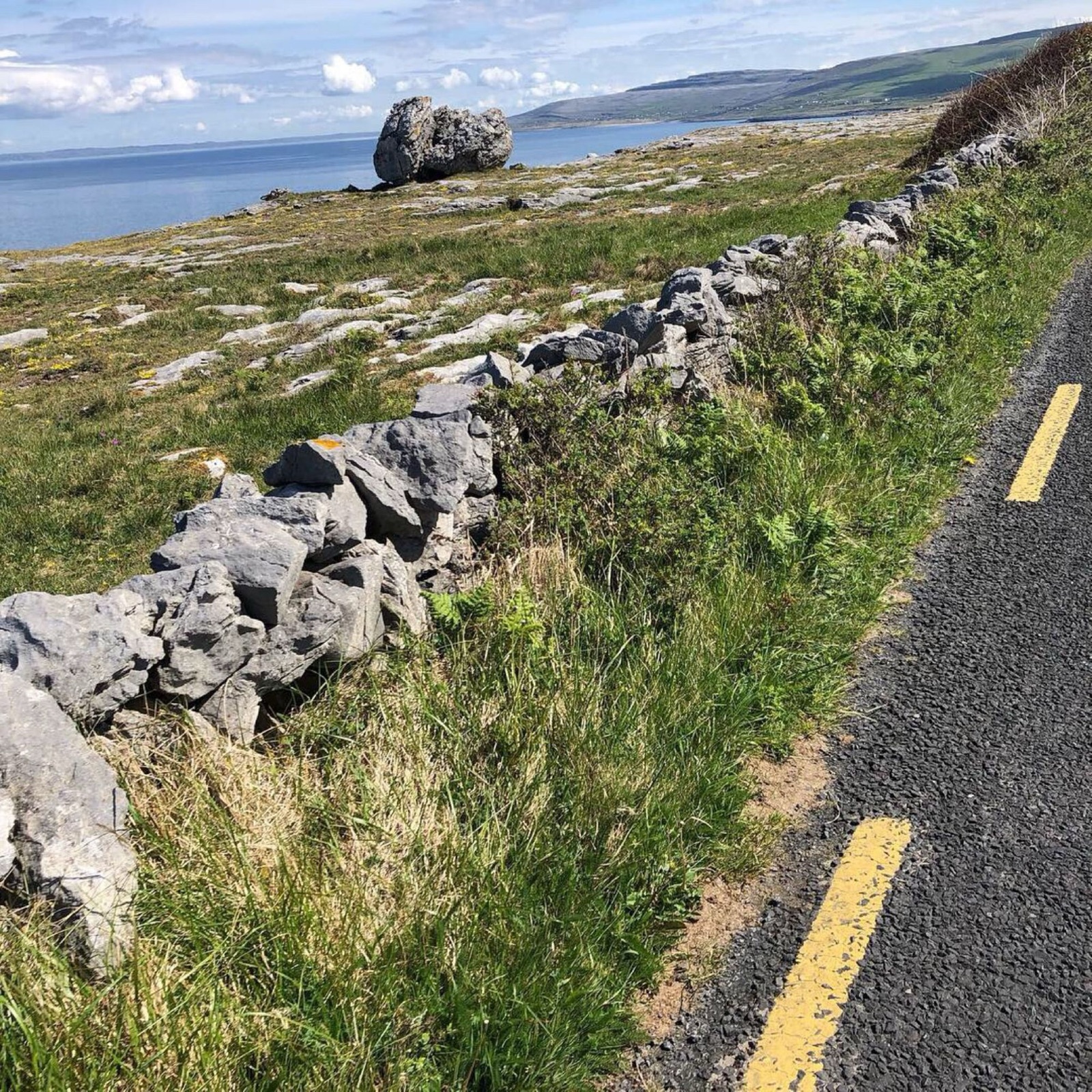 The Burren coastal road in County Clare, with a limestone dry-stone wall and a glacial erratic boulder overlooking Galway Bay
