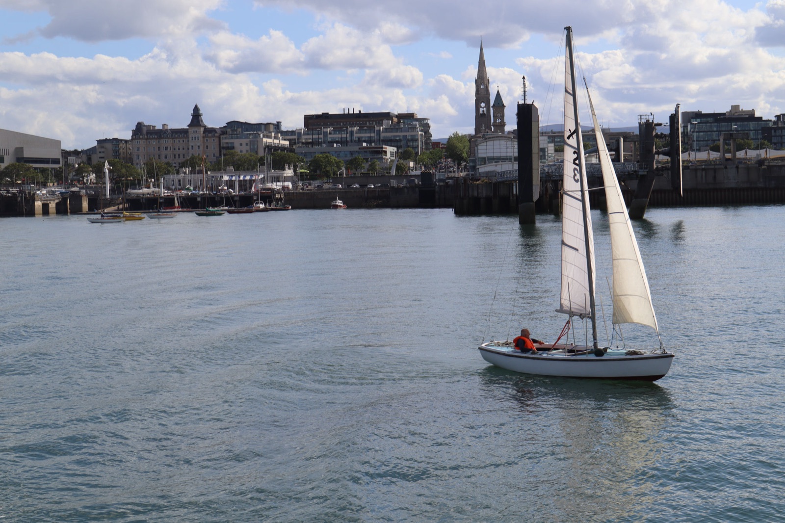 A dinghy sailing in Dún Laoghaire harbour, with the town and the spire of the Mariners' Church (National Maritime Museum) behind