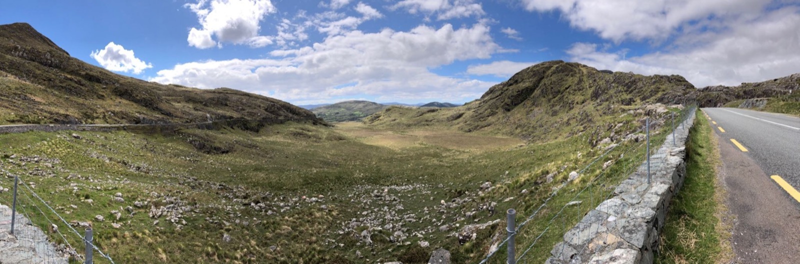 A mountain pass road winding through a glaciated upland valley in County Kerry, with dry-stone walls and open moorland