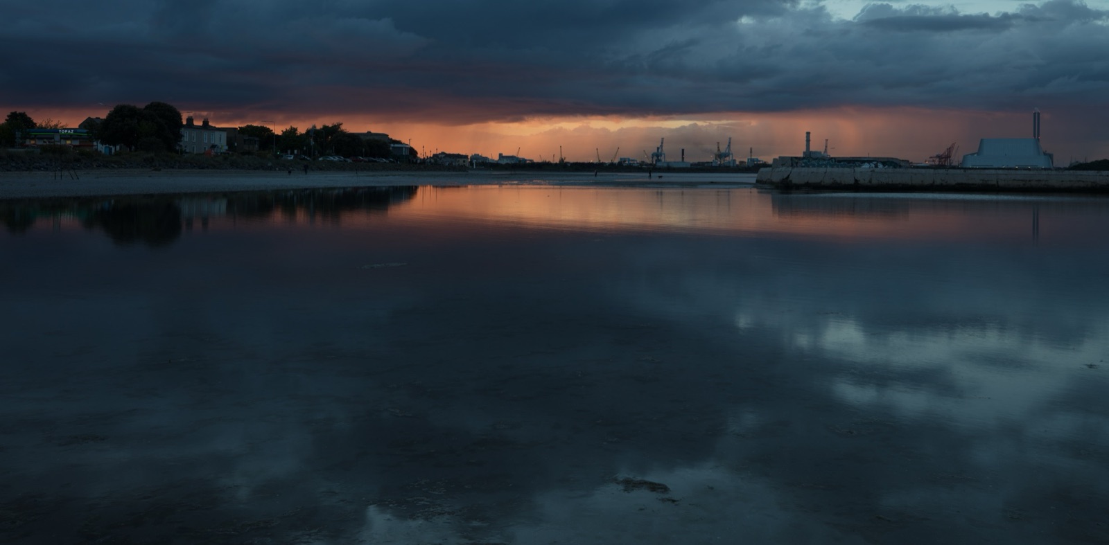 Sunset over Sandymount Strand at low tide, with the Poolbeg chimneys and Dublin Port cranes on the horizon reflected in the wet sand