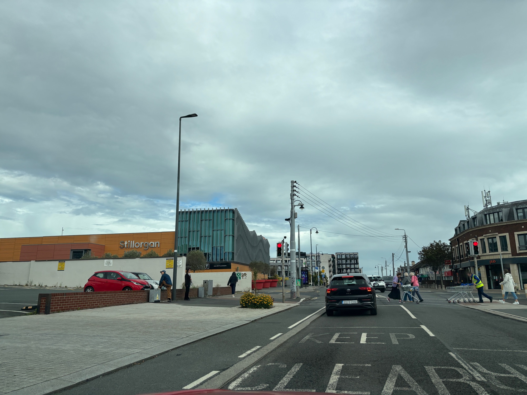 Stillorgan Shopping Centre, with its landmark orange sign, seen across the junction at the village centre, with a Permanent TSB branch and shoppers crossing to the right